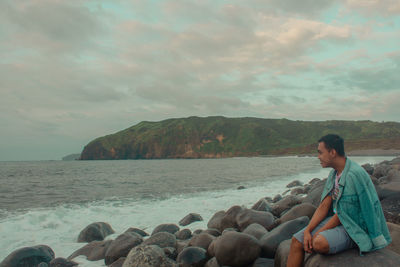 Woman sitting on rock by sea against sky