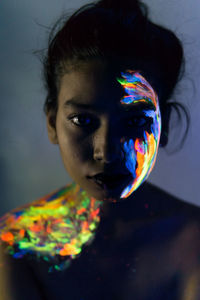 Close-up portrait of young woman with paint on face and body in darkroom