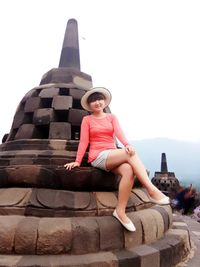 Full length of young woman sitting outdoors against clear sky