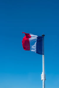 French flag on the mast over a blue sky.