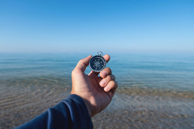 Compass in a man's hand against the background of the morning sea and pebble beach. travel by sea