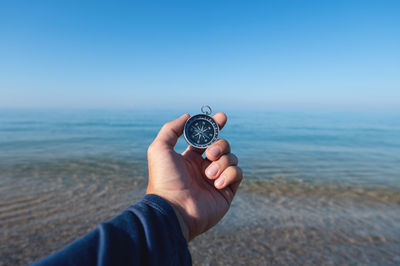 Midsection of person holding sea against blue sky