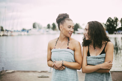 Smiling daughter and mother in swimwear talking while standing against lake