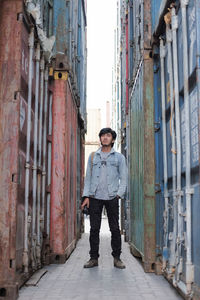 Full length of man holding camera while standing amidst cargo containers