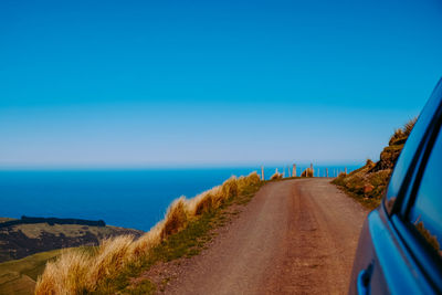 Scenic view of road by sea against clear blue sky