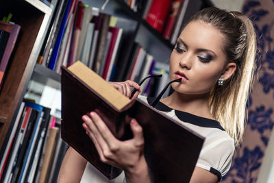 Woman reading book by shelf at library