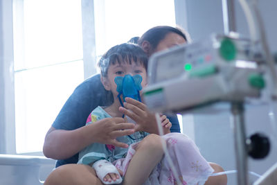 Portrait of cute son wearing oxygen mask with mother in hospital
