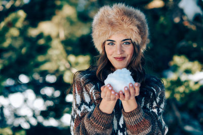 Portrait of beautiful woman holding snow while standing against trees