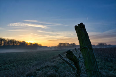 Wooden posts on field against sky during sunset