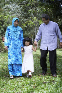 Smiling girl walking with grandparents on grass in back yard