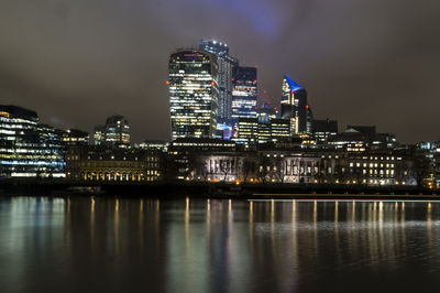 Illuminated buildings by river against sky at night