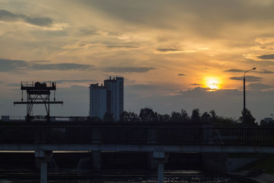 Silhouette buildings by river against sky during sunset