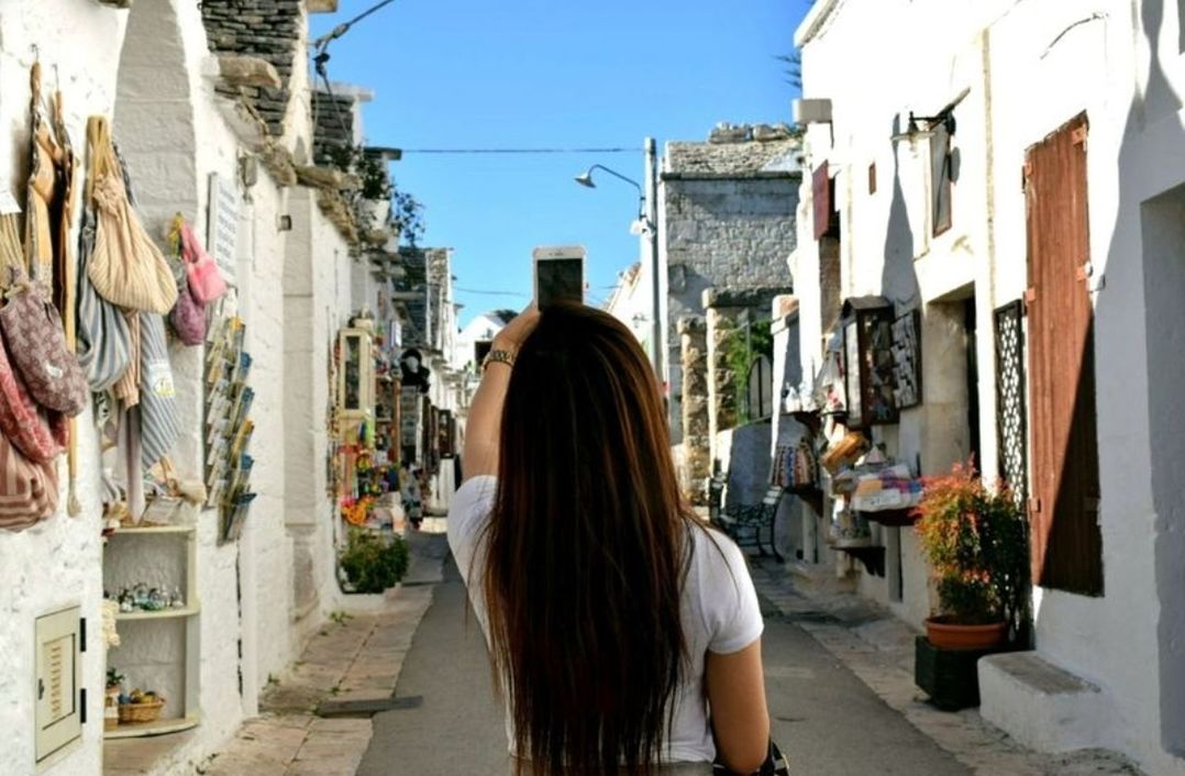 REAR VIEW OF WOMAN STANDING ON STREET AMIDST CITY