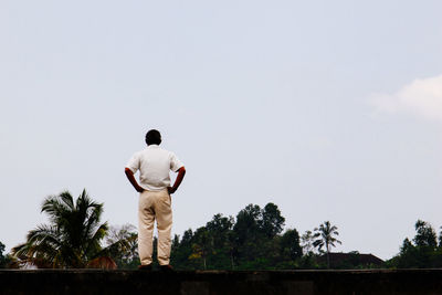 Rear view of man with hands on hip standing against clear sky