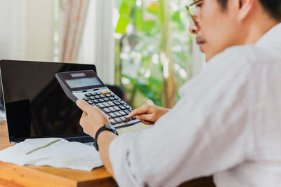 Midsection of man using calculator while sitting on table