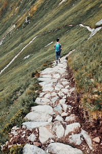 Young man with backpack hiking in a mountains, actively spending summer vacation