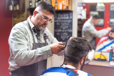 Barber cutting male customer hair in salon