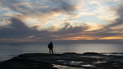 Silhouette standing on beach against sky during sunset