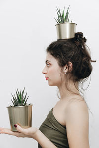 Side view of woman holding potted plant against wall