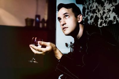 Young man looking up holding wine glass