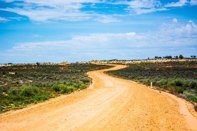 Dirt road passing through landscape against sky