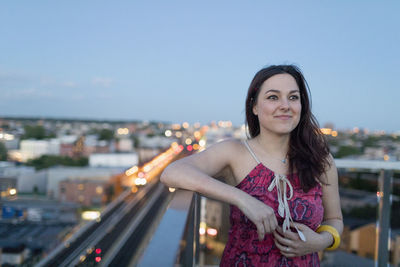 Portrait of smiling woman standing against sky in city