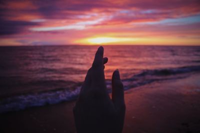 Cropped hand of woman at beach against cloudy sky during sunset