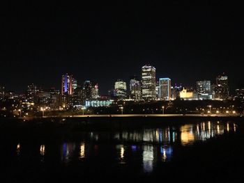 Illuminated cityscape by sea against sky at night