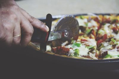 Cropped hand cutting pizza with pizza cutter
