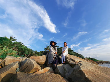 People sitting on rock against sky