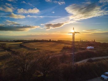 Electricity pylon on landscape against sky during sunset