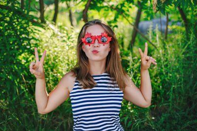 Portrait of young woman wearing sunglasses standing against plants