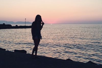 Silhouette woman standing on beach against sky during sunset