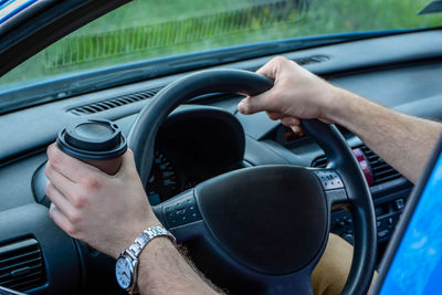 Cropped image of man holding coffee cup while driving car
