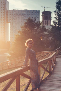 Woman leaning against railing while standing in city during sunset