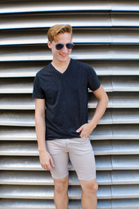 Portrait of young man wearing sunglasses standing against shutter