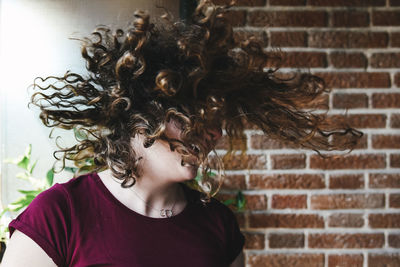Happy young woman tossing hair against wall