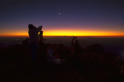 Silhouette people on mountain against clear sky during sunset