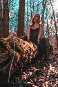 Young woman looking away while sitting on tree trunk in forest