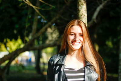 Portrait of smiling woman against trees in sunny day