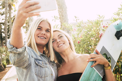 Smiling friends taking selfie with skateboard in park