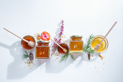 Composition of honey jars with honey sticks, flowers and bee pollen on white background.