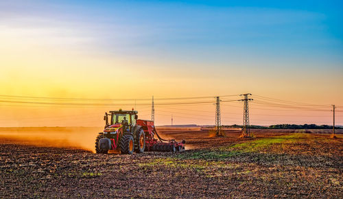 Tractor on agricultural field against sky during sunset
