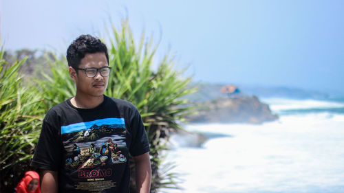 Young man standing at beach against sky