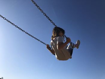 Rear view of girl on swing at playground against clear blue sky