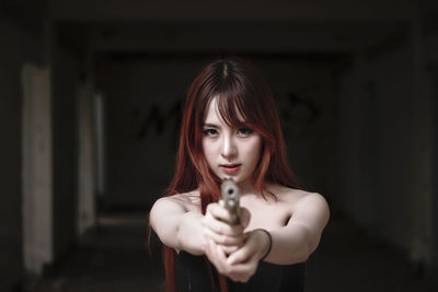 Portrait of young woman shooting with handgun in darkroom