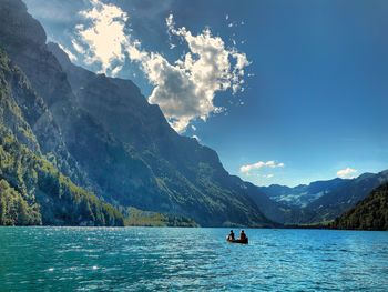 People on lake by mountains against sky