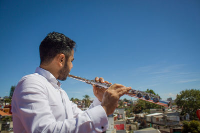 Flautist on the roof toop playing with blue skye on the background