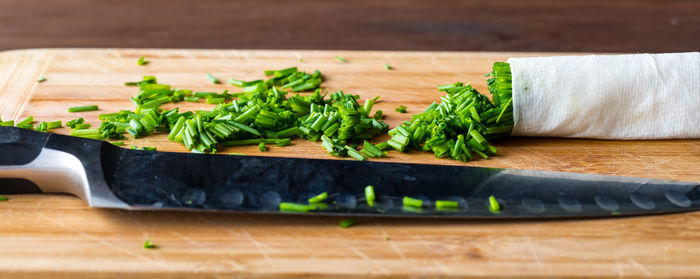 A narrow view of a pile of chopped chives with a sharp knife in front.