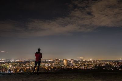 Rear view full length of man standing against illuminated cityscape at night